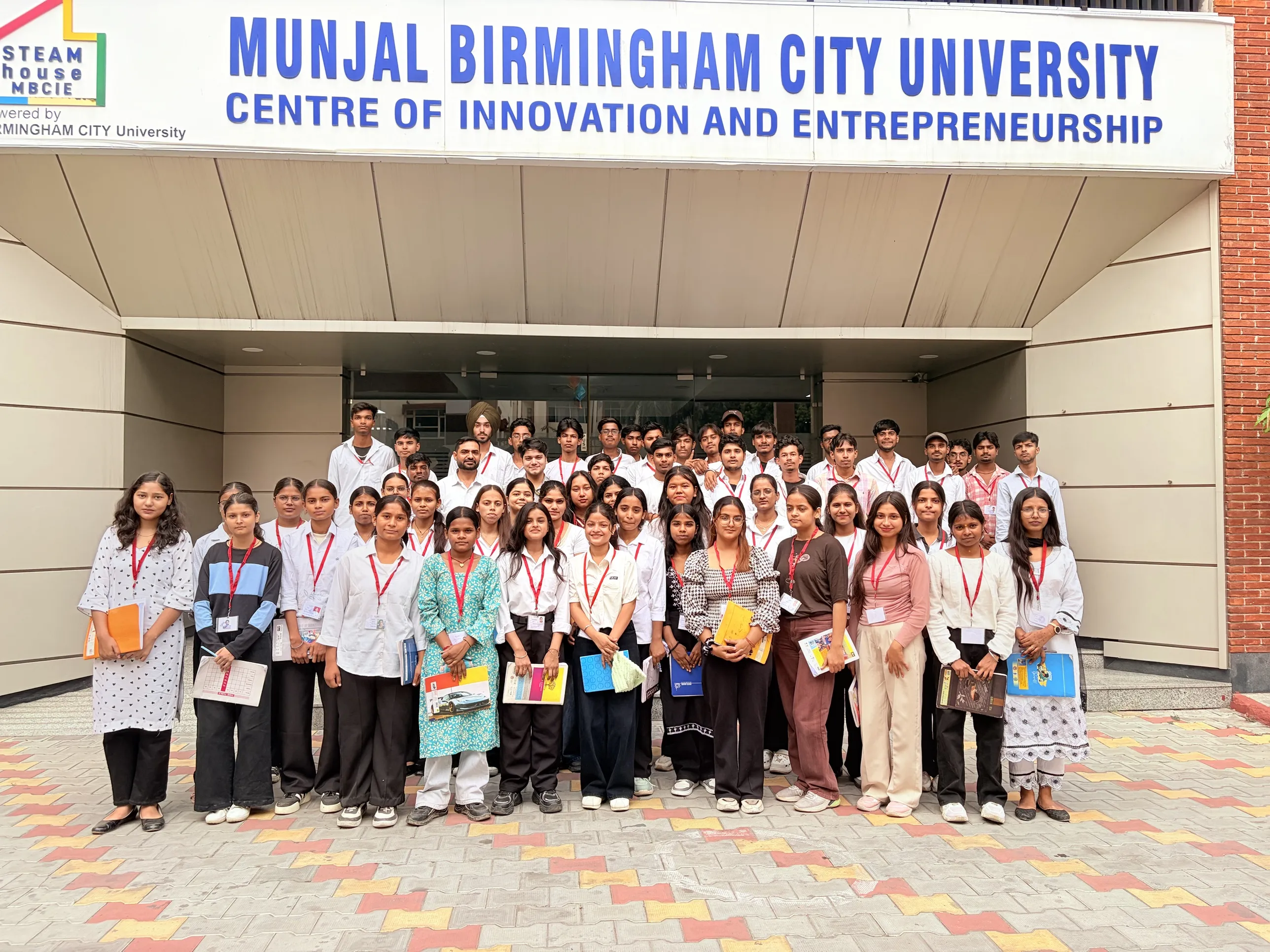 BCA and B.Sc IT first-year students holding notebooks and wearing red ID lanyards, posing in front of the Munjal Birmingham City University Centre of Innovation and Entrepreneurship entrance in Ludhiana