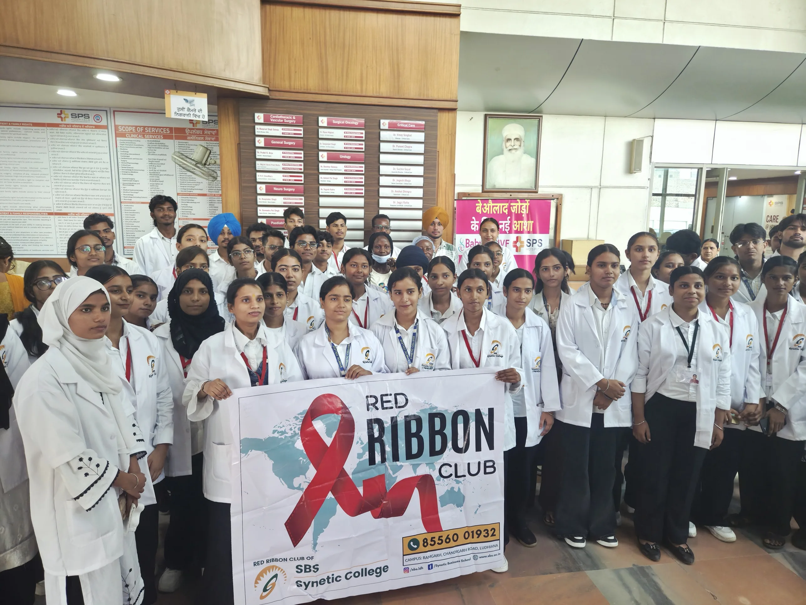 B.Sc MLS students in white lab coats gathered in the SPS Hospitals lobby holding the Red Ribbon Club of SBS Synetic College banner